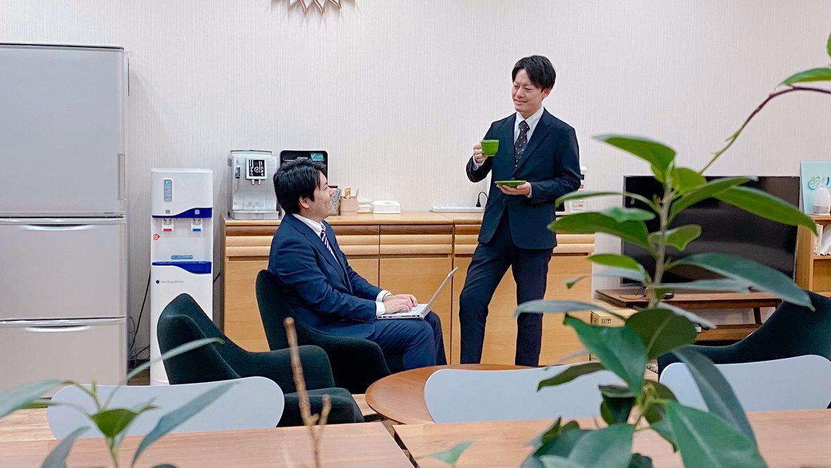 ウォーターサーバーの前でコーヒーを飲みながら話す社員